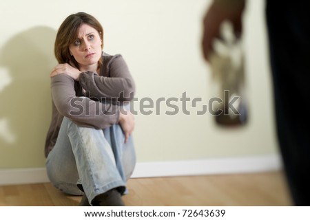 Woman scared of a man holding a bottle; Concept: abuse/domestic violence due to alcoholism