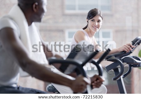 Two people speaking together while biking at health club, foucs on the girl