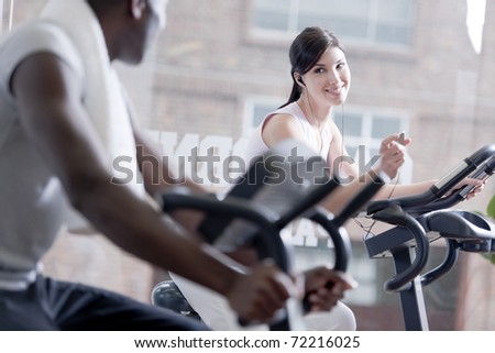 Two people speaking together while biking at health club, focus on the girl