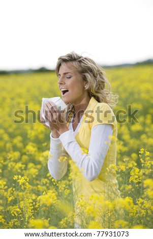 Young woman sneezing in a flowers meadow. Concept: seasonal allergy.