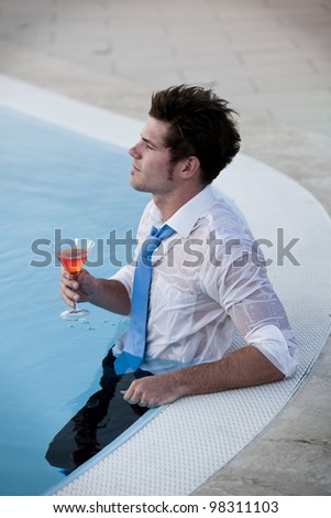 Young man having a drink in the pool, his clothes on