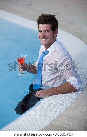Young man having a drink in the pool, his clothes on