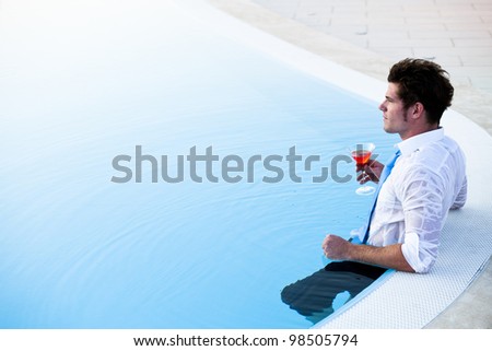 Young man having a drink in the pool, his clothes on, lots of copy-space
