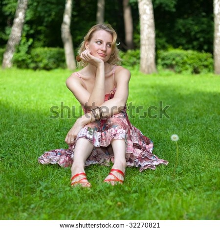 Girl sits on a lawn, supports her face by hand and looks sideways