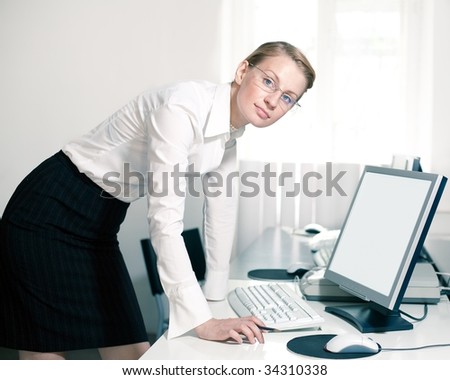 Young woman stays by computer and looks at camera