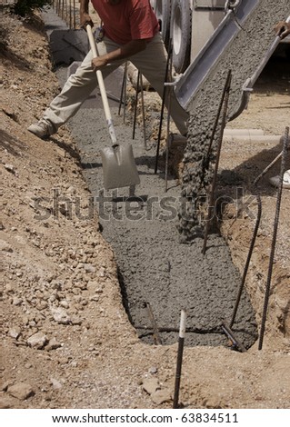 Truck with worker pouring concrete into form. Focus on shovel and hands.