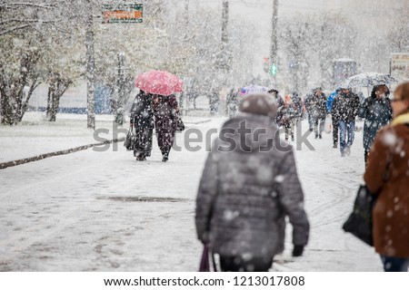 the city was covered by a snow storm, cold, climate change, movement is paralyzed because of the snow people move to the snowstorm on foot, hiding umbrellas and hoods, abnormal winter, precipitation