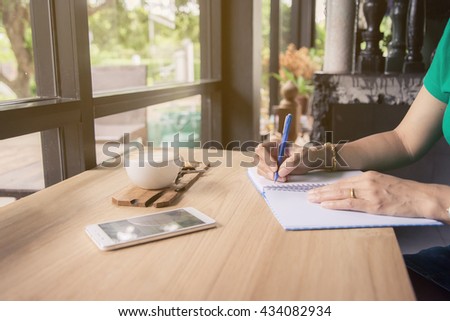 Girl writing in a notebook with cell phone and cup of coffee on a wooden table
