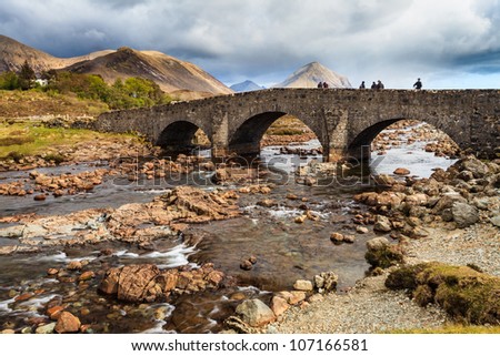 People standing on a bridge over a river with mountains in the background