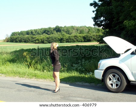 blonde girl in business suit standing in middle of road on her cell phone next to broken down vehicle on the side of the road