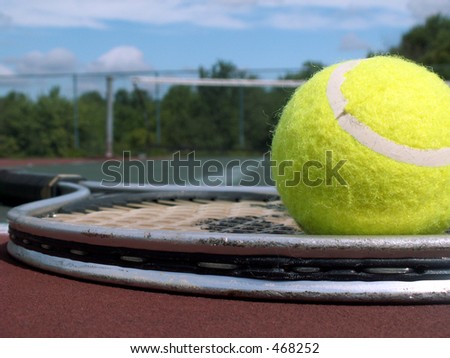 tennis ball resting on a raquet at the edge of a tennis court.