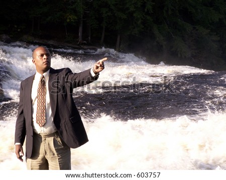 business man in a suit standing in front of a rushing river with finger pointing