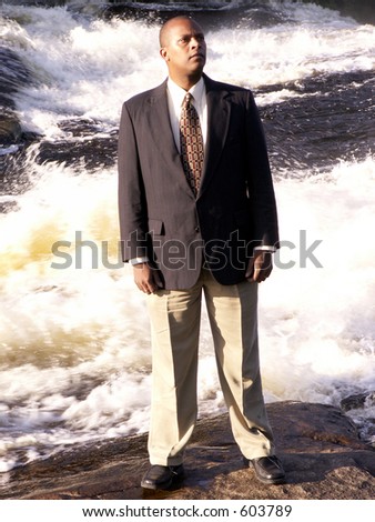 business man in a suit looking a little bewildered standing on a rock in front of a rushing river