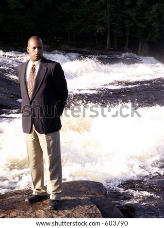business man in a suit standing on a rock in front of a rushing river