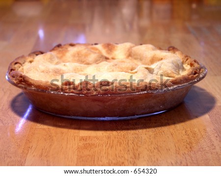 freshly baked apple pie on a butcher block table. focus on leading edge of pie. shallow depth of field.