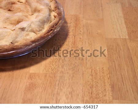 corner of a freshly baked apple pie on a butcher block table. focus on leading edge of pie. shallow depth of field.