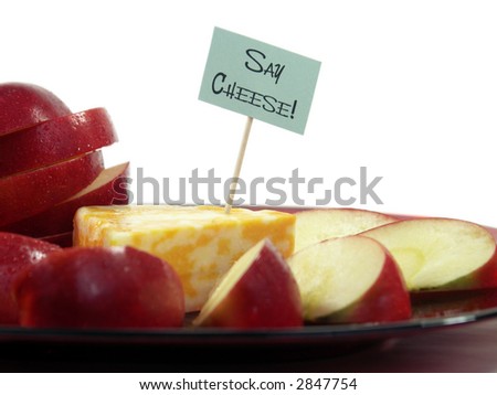 Wedge of colorful cheese with a toothpick sign and apple slices on a red plate isolated on white. Shallow DOF, focus on sign.