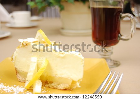 Lemon pie on a yellow plate with coffee in the background on a restaurant table.