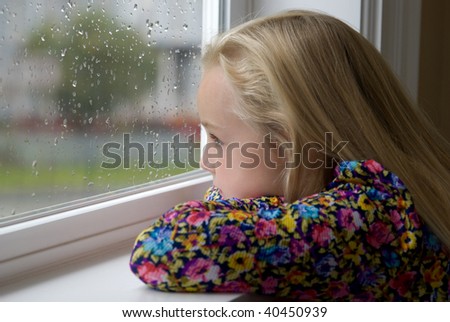 A young blond girl sits looking out the rainy window