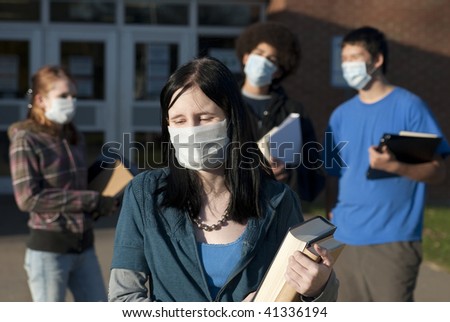 Students of various ethnic backgrounds wearing masks in front of a school. Focus on teen girl in front.