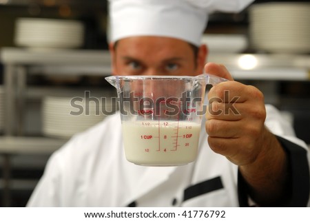 Attractive Caucasian chef looks a milk in a measuring cup. Shallow DOF. Focus on measuring cup.