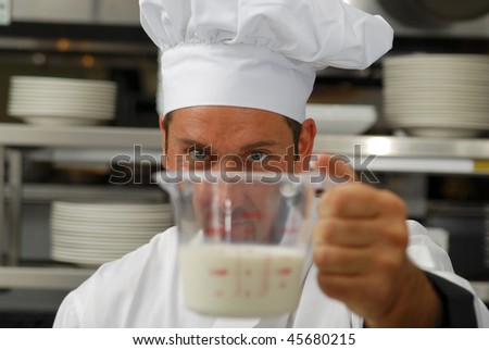 Attractive Caucasian chef looks a milk in a measuring cup. Shallow DOF. Focus on face.