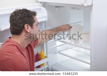 Attractive Caucasian male reaching into a sparse refrigerator
