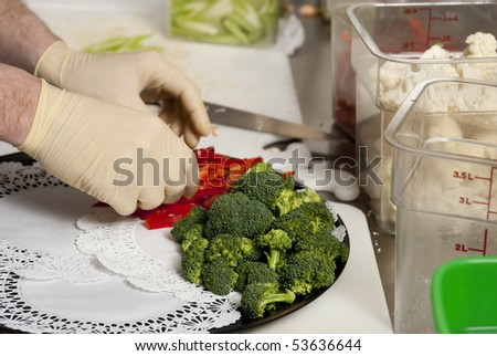 A food service worker places broccoli on a tray