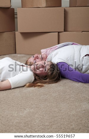 Female roommates lying on the floor in front of moving boxes.