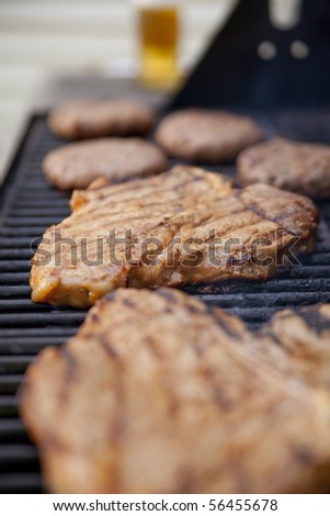 Steaks and burgers on the grill with a bottle of beer out of focus on the background. Shallow DOF on the second steak.