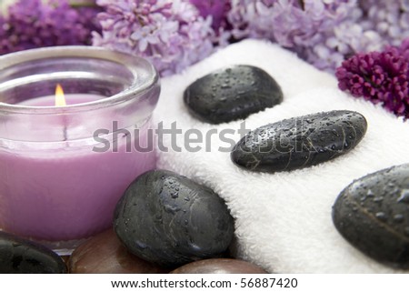 Rocks with water droplets on a white towel with a purple candle and lilac flowers.