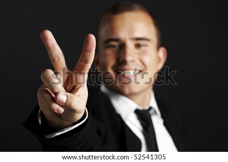 Young business man on black background shows the peace sign