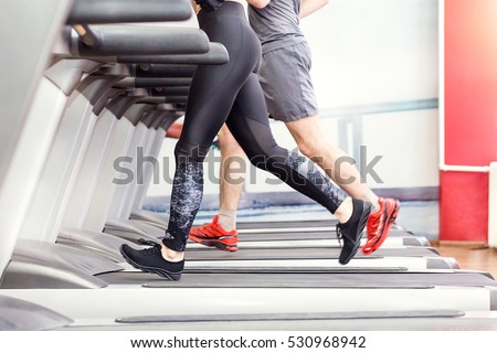 Sport, fitness, lifestyle, technology and people concept - close up of woman and men legs walking on treadmills in the gym.