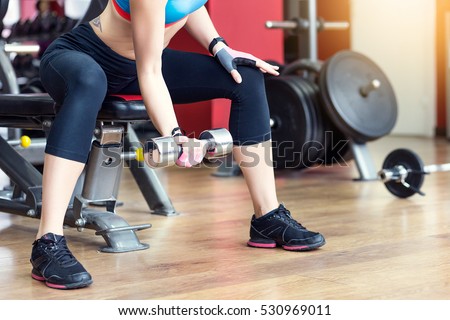 Close-up of a young woman exercising with weights in the gym. Fit girl with dumbbell. Sport and fitness concept