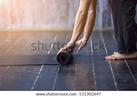 Yoga concept. Young yogi men rolling mat after a yoga on black wooden floor