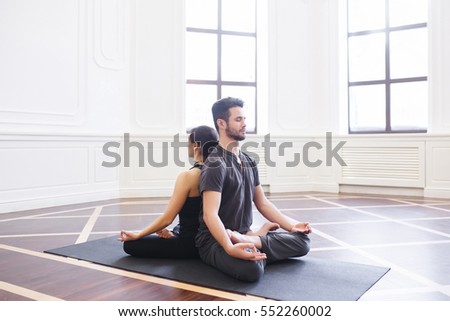 Yoga group concept. Young couple meditating together, sitting back to back on windows background