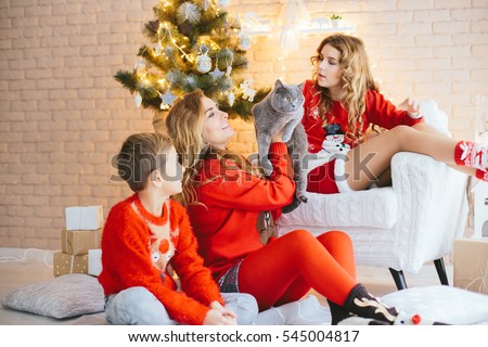 Very beautiful young boy and girl with her mother in a red sweater and red socks with a cat sitting on their hands in anticipation of the New Year. Family happiness ...