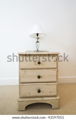 detail of a wooden bedside table with three drawers and reading lamp
