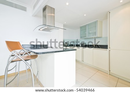 Modern fully fitted kitchen in vanilla white with breakfast bar and orange chairs