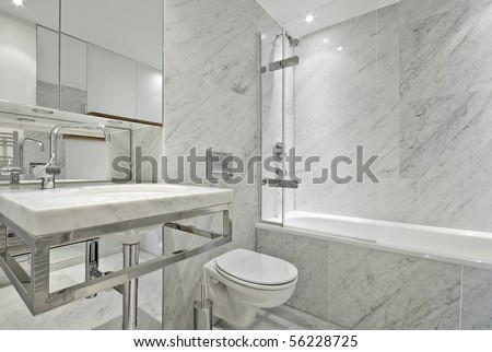 Modern and contemporary en suite bahroom in marble white with designer fragments, large bath tub, stylish wash basin and toilet