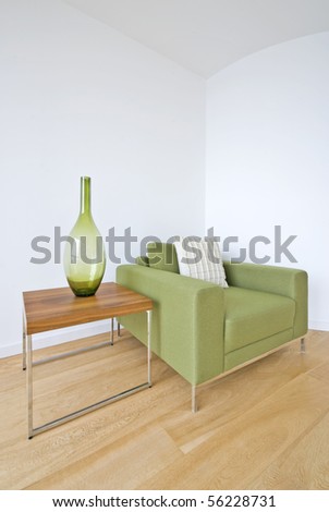 Detail of a modern living room with designer green armchair, wooden coffee table and decorative vase
