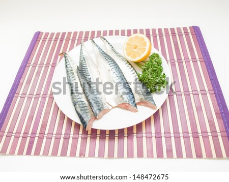 Raw mackerel fish filet on white plate, half a lemon and parsley on the side on purple wooden table cover