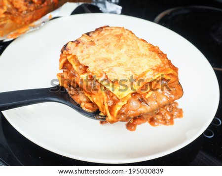 Someone plating fresh lasagna onto porcelain plate with black spatula