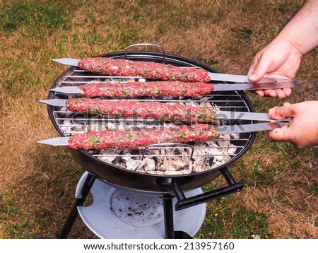 A chef putting red meat shish kebab onto a charcoal barbecue