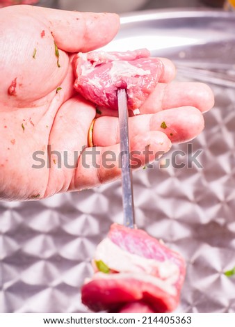 Closeup of a chef entering pieces of meat onto a skewer, making shish kebab