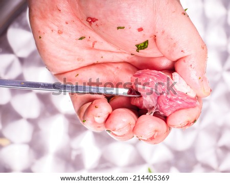 Closeup of a chef entering pieces of meat onto a skewer, making shish kebab