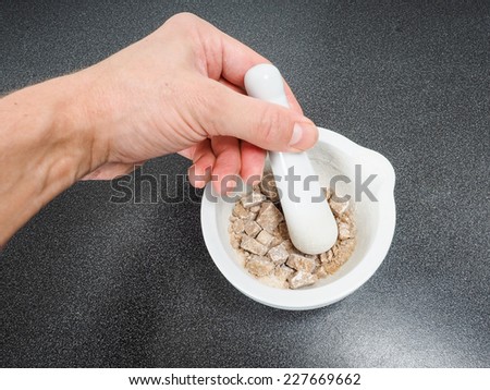 Person crushing brown sugar cubes in a white marble mortar on black table