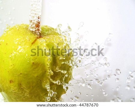 A green apple under a water fall, water drops bouncing off and frozen in midair