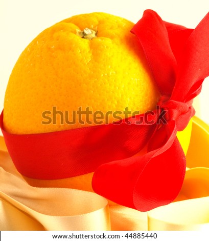 An orange fruit with a red bow around, with white background and a golden ribbon in front