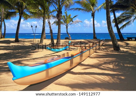 Outrigger canoe sits on a picturesque sandy beach among palm trees, with the ocean beyond